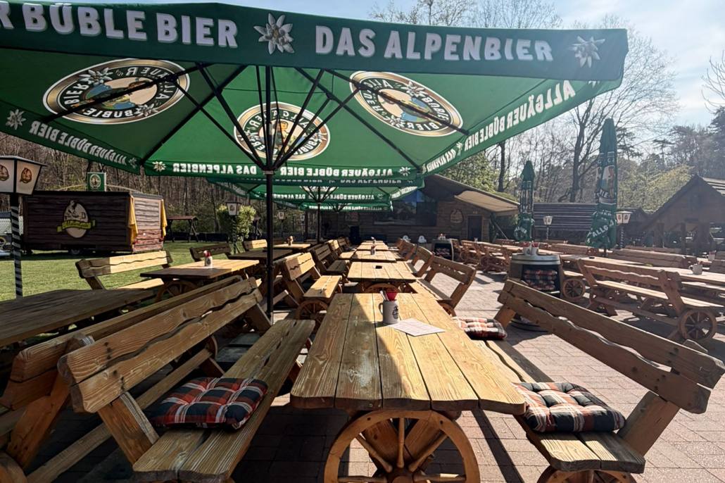 Biergarten mit Holztischen und Bänken unter grünen Sonnenschirmen