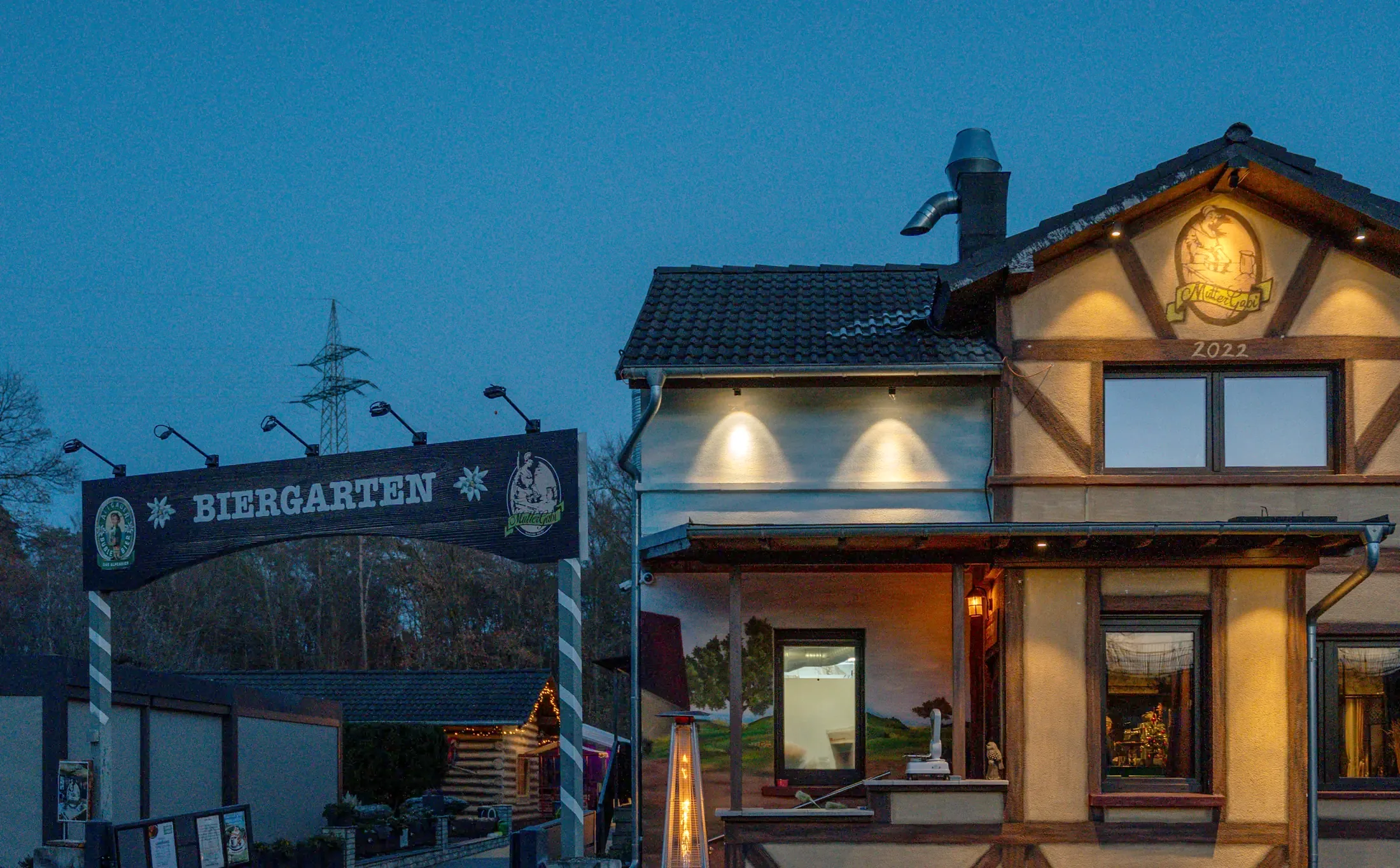 Das Fachwerkhaus von Mutter Gabi mit beleuchtetem Logo am Giebel zur blauen Stunde