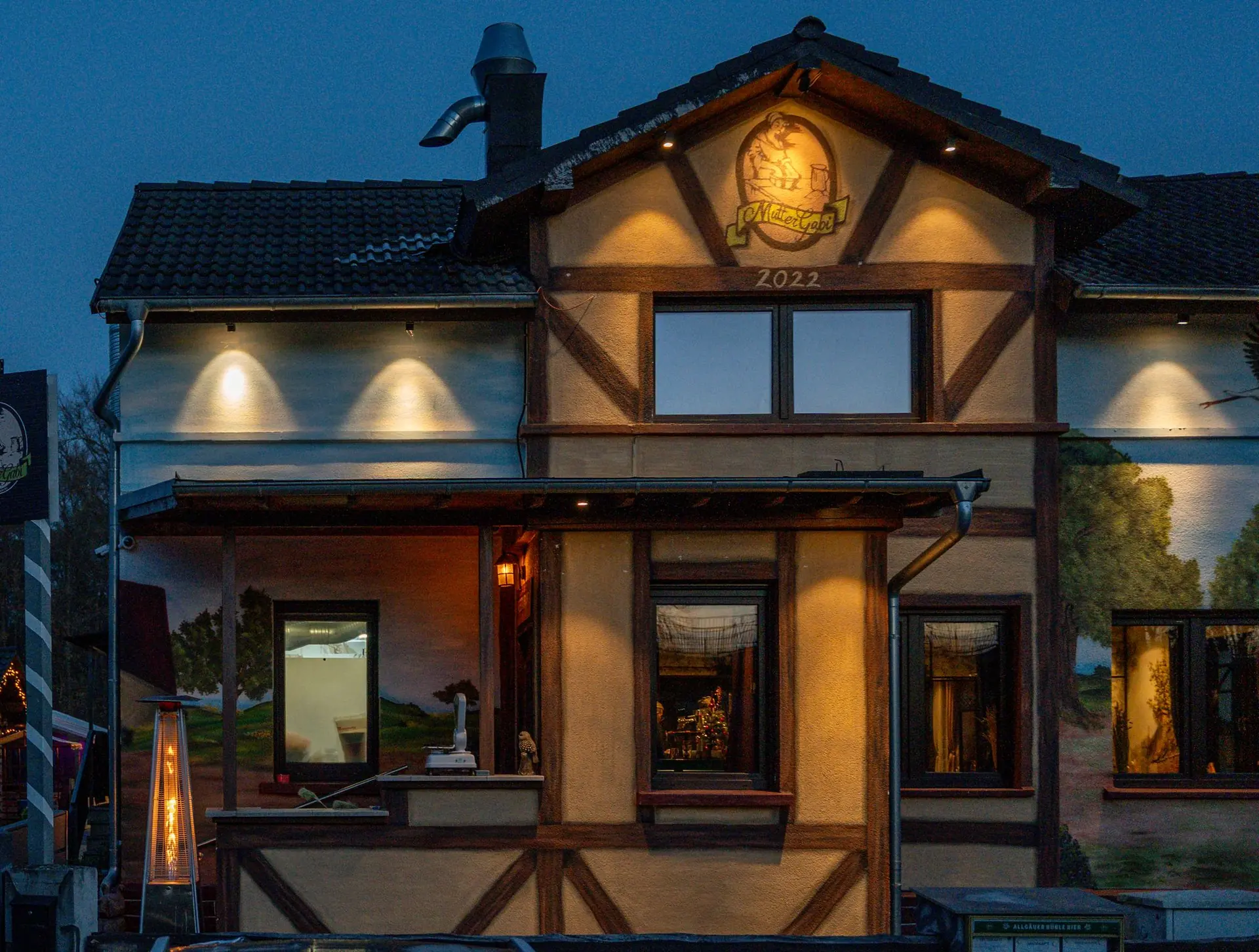 Das Fachwerkhaus von Mutter Gabi mit beleuchtetem Logo am Giebel zur blauen Stunde