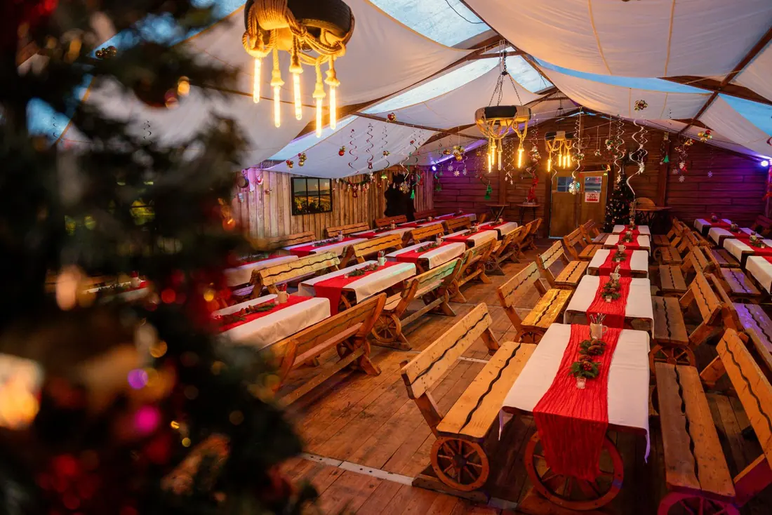 Festzelt in der Adventszeit mit langen Holztafeln, roten Läufern und Tannengrün