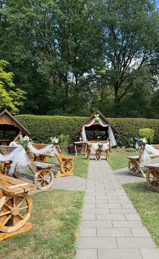 Für eine freie Trauung geschmückter Garten mit Holzbänken, Tüll und Hütte