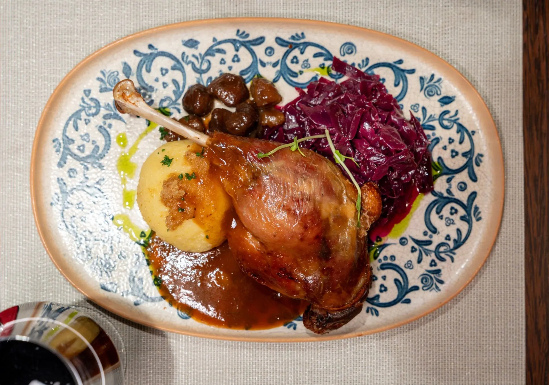 Gänsekeule mit Knödel, Apfel-Rotkohl und Maronen auf blau-weißem Teller