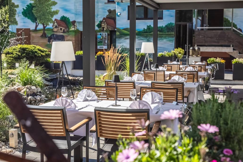 Gedeckte Tische unter der Pergola zwischen Blumen