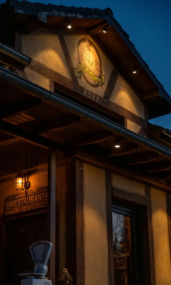 Giebel mit dem Mutter-Gabi-Logo und dem beleuchteten Restaurant-Schild am Abend
