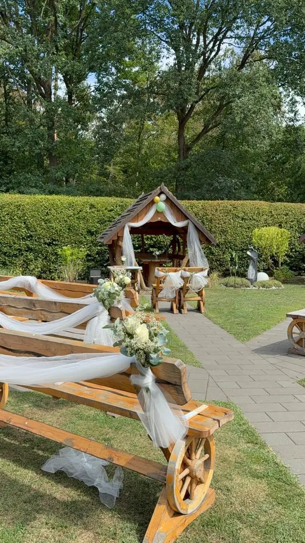 Holzbank mit Wagenrad, Blumenstrauß und weißem Tüll im Garten