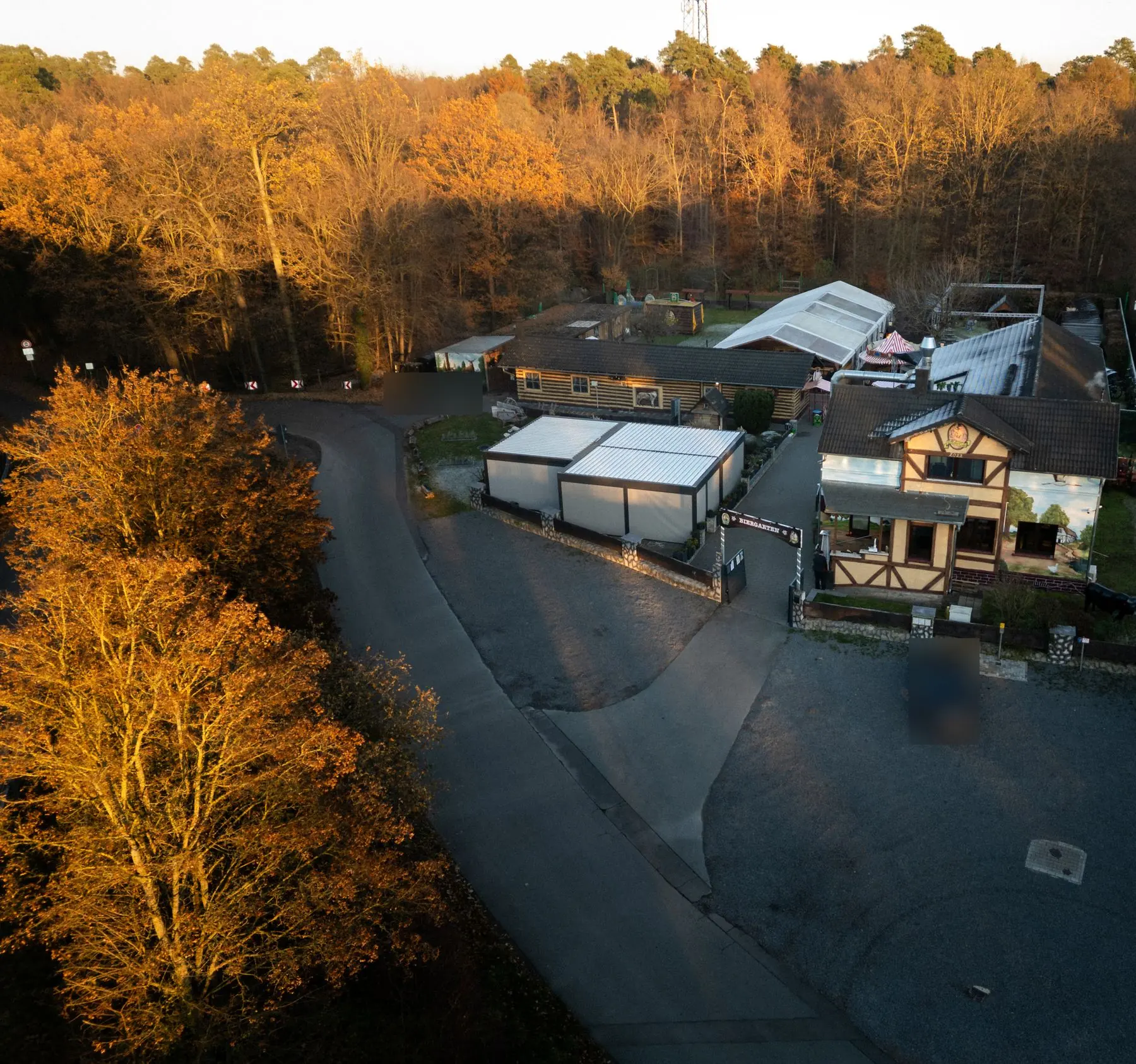 Luftaufnahme von Mutter Gabi im Herbstlicht: Fachwerkhaus, Biergarten-Eingang, Festzelt und Parkplatz am Waldrand