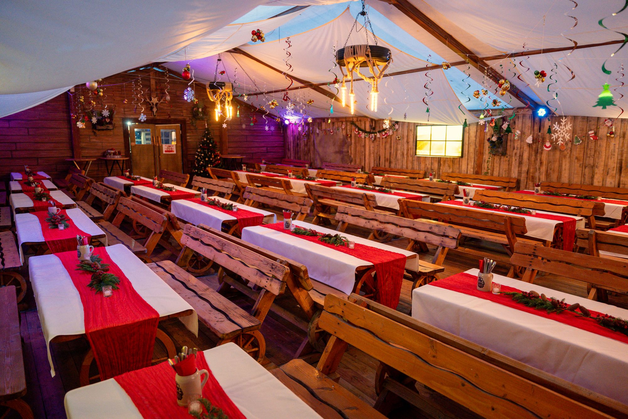 Weihnachtlich eingedecktes Festzelt mit weißen Tischdecken, roten Läufern und Leuchtern